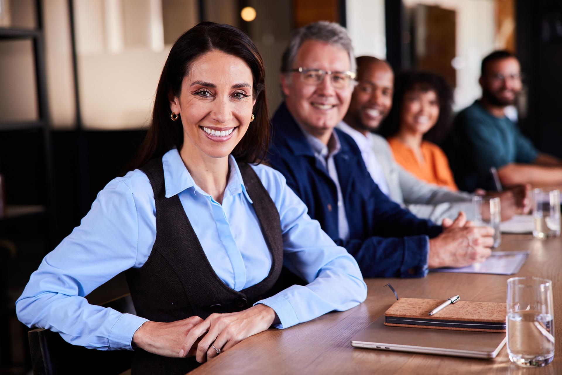 Businesswoman and a diverse group of coworkers smiling at a board room table